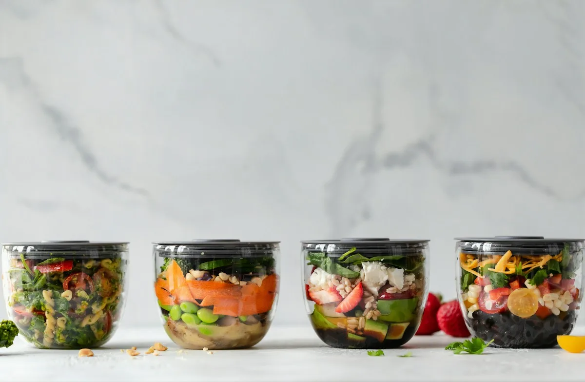 Four glass food containers holding layers of vegetables